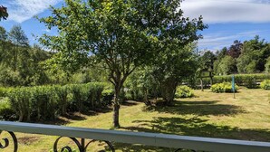 A garden with a variety of trees and shrubs, a clear sky, and a metal railing in the foreground. - Holiday cottage tummel valley beautiful views. Own garden dog friendly  (Pershire)