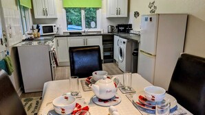 A compact kitchen with white cabinets, a microwave, a washing machine, and a refrigerator. - Holiday cottage tummel valley beautiful views. Own garden dog friendly  (Pershire)