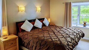 A bedroom with a large bed, two bedside lamps, a nightstand, and a window with curtains. - Holiday cottage tummel valley beautiful views. Own garden dog friendly  (Pershire)