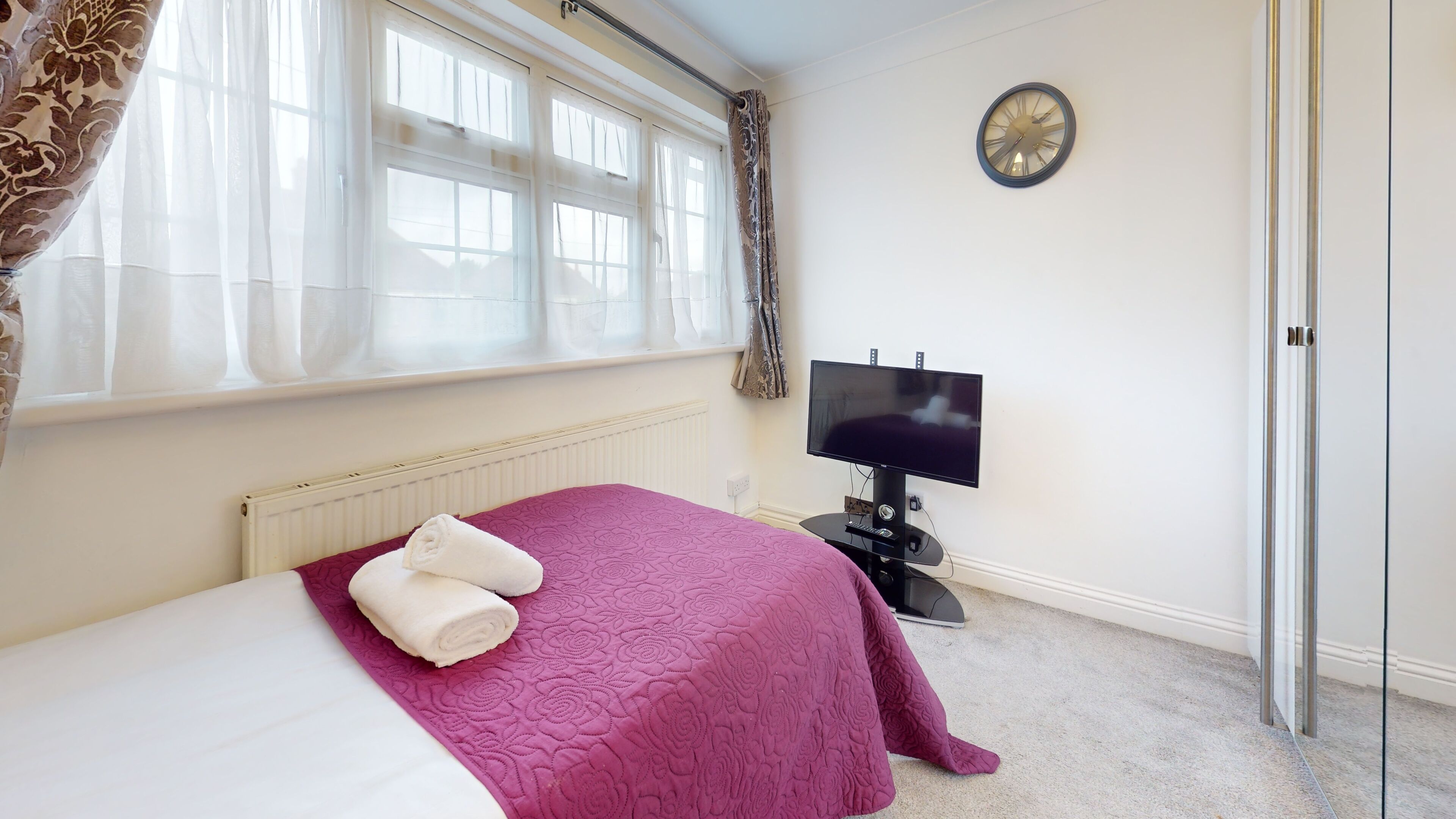 A bedroom with a bed, a TV, and a window with curtains.