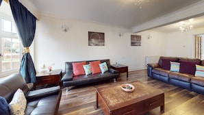 A spacious living room with a black leather sofa, a wooden coffee table, and a blue leather sofa. - Charming 5-bed House in Grays (Grays)