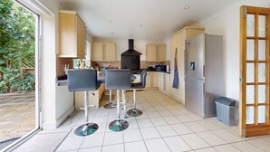 A modern kitchen with a central island, bar stools, a built-in oven, and a large refrigerator. - Charming 5-bed House in Grays (Grays)