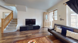 A living room with a staircase, a television on a black stand, a leather sofa, and a wooden floor. - Charming 5-bed House in Grays (Grays)