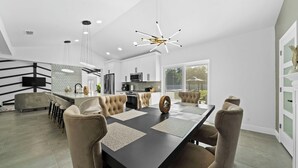 Una cocina moderna con armarios blancos, una isla central y un comedor con mesa negra y sillas color beige.