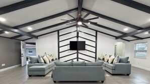 Un salón amplio con un ventilador moderno en el techo, sofás grises y un televisor de pantalla plana montado en la pared.
