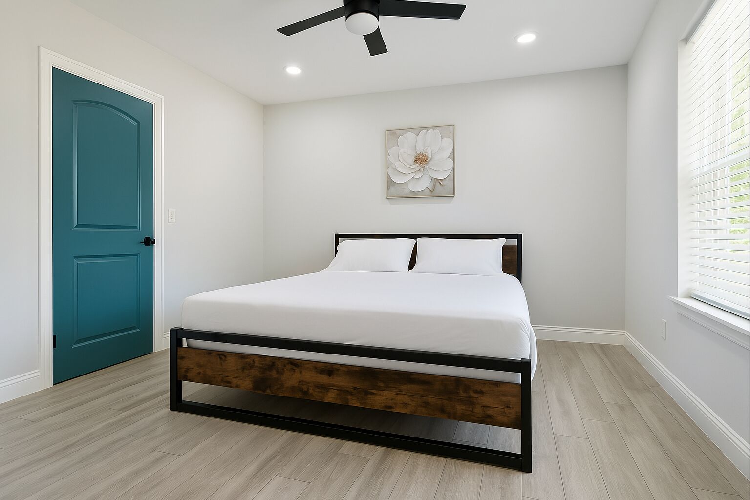 Ein Schlafzimmer mit Bett, Deckenventilator, Fenster mit Jalousien und einer Tür.