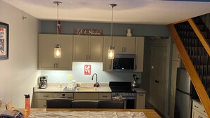 Una cocina compacta con una mesa de comedor, dos lámparas colgantes, un microondas y un refrigerador.