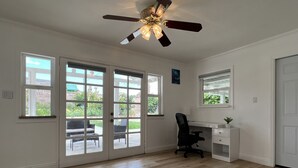 A spacious room with a ceiling fan, large windows, a desk, and a chair.