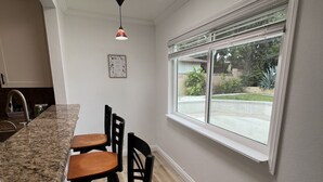 A kitchen with a granite countertop, wooden chairs, a window with blinds, and pendant lighting.
