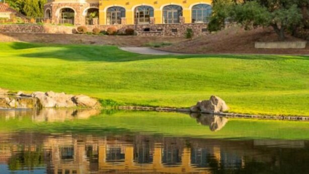 A golf course with a pond reflecting a building with arched windows.