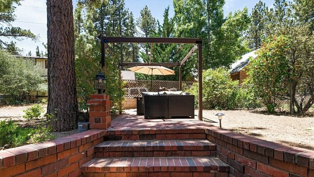 Eine Ziegelsteintreppe führt zu einem überdachten Außenbereich mit Pergola und Tisch und Stühlen darunter.