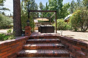 Una scala in mattoni conduce a una zona salotto esterna coperta, con una pergola e un tavolo e sedie sotto.