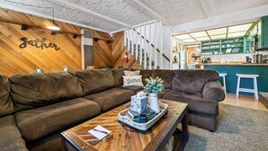 Ein gemütliches Wohnzimmer mit zwei braunen Sofas, einem Holztisch und einer Küchenzeile im Hintergrund.