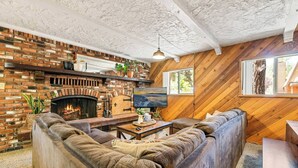 Ein gemütliches Wohnzimmer mit Kamin aus Backstein, einer großen Eckcouch und Holzwänden.