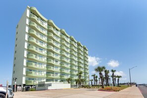 Un hotel de varios pisos con balcones, un estacionamiento y palmeras.