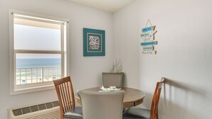 Un comedor con una mesa redonda, dos sillas de madera, una ventana con vistas al océano, una obra de arte enmarcada y un adorno de pared.