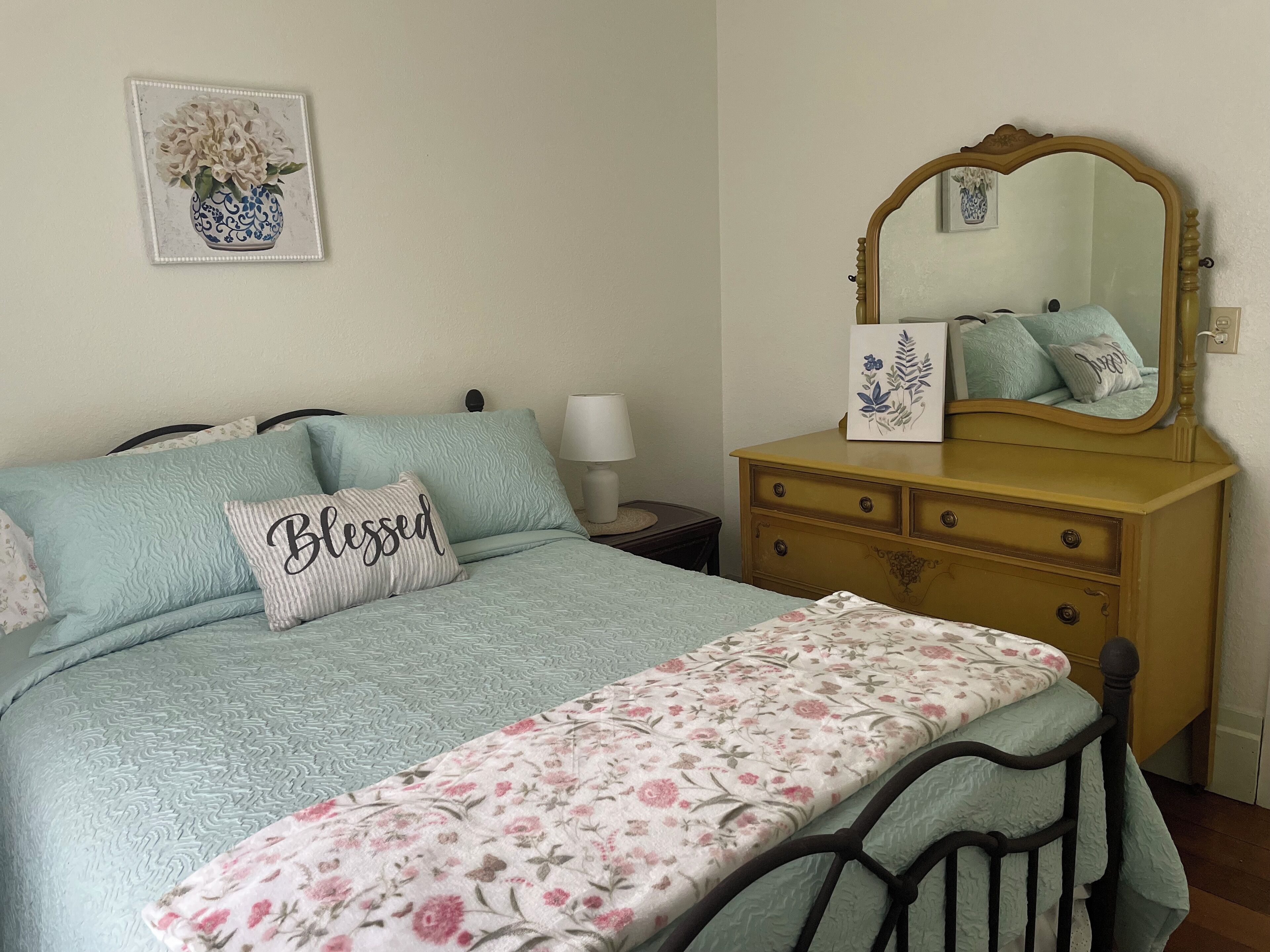 A bedroom with a bed, a dresser, a mirror, a nightstand, and a wall-mounted picture.