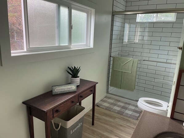 A bathroom with a glass shower enclosure, a wooden vanity with a plant, and a sign saying "Everything is possible." - Downtown Boonville Vintage Farmhouse (Boonville)