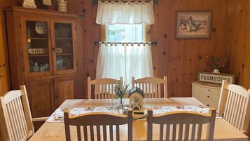 A wooden dining room with a table, chairs, a cabinet, and a window with curtains.