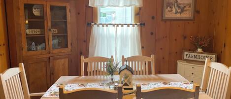 A wooden dining room with a table, chairs, a cabinet, and a window with curtains.