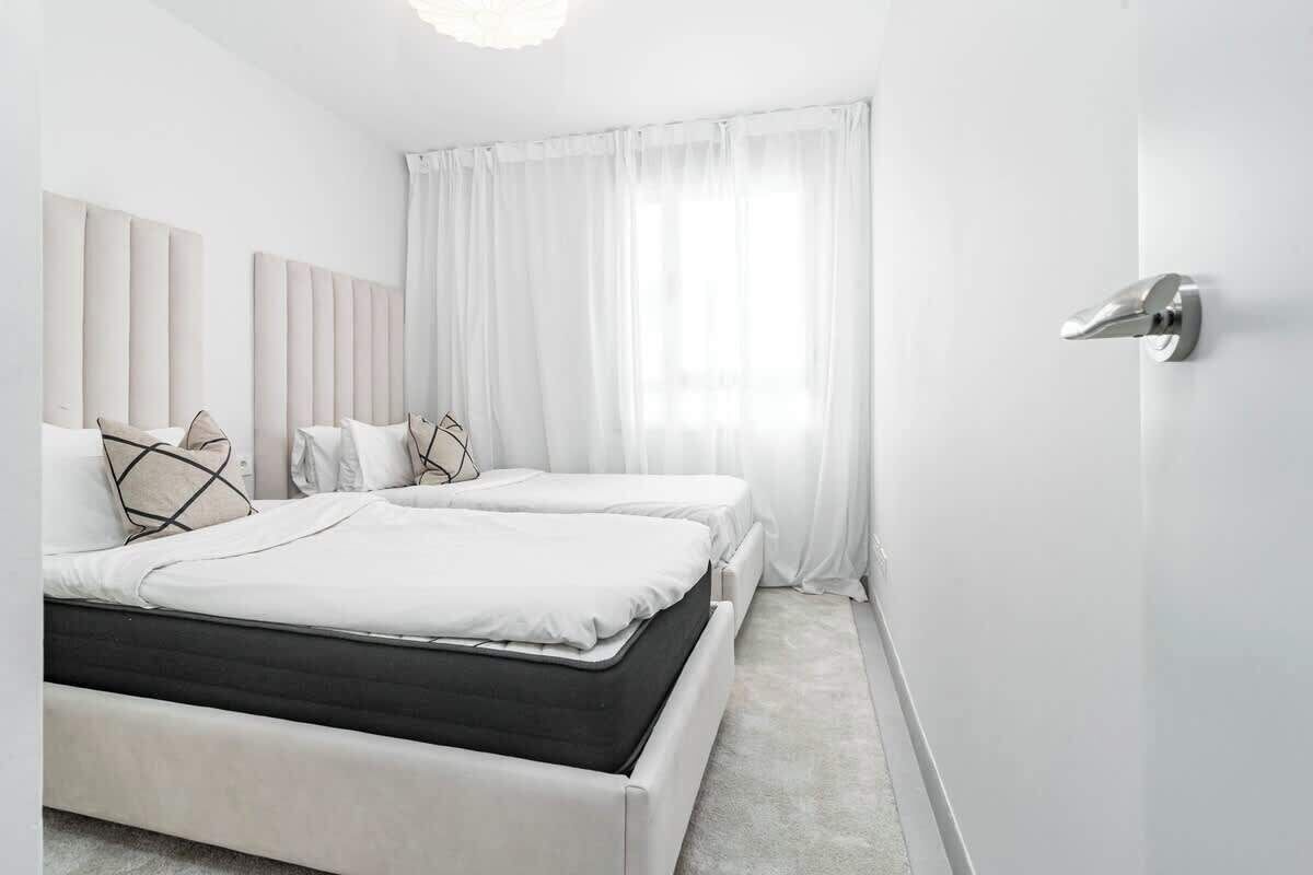 A modern bedroom with two beds, white bedding, and a large window with sheer curtains.