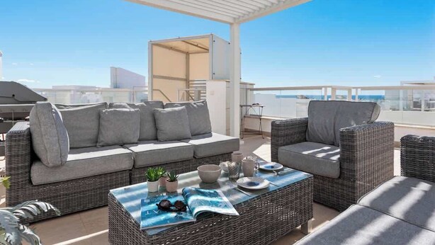 A rooftop terrace with a grey sofa, wicker chairs, and a table with a magazine and decorative items. - Penthouse with sea views in San Pedro de Alcántara by Costarentals - Ref M34 (San Pedro Alcántara)
