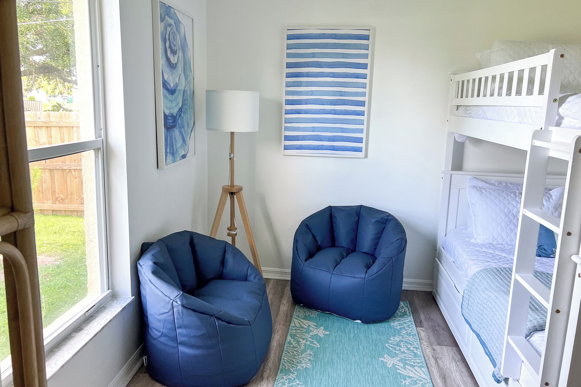A room with a bunk bed, two bean bag chairs, a floor lamp, and a painting on the wall.