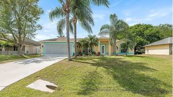 A residential property with a single garage, a well-maintained lawn, and several palm trees.
