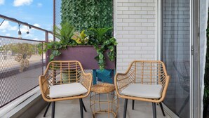 A balcony with two wicker chairs, a potted plant, and a white brick wall. - Luxury Mid-century Condo, Cozy & Fully Remodeled. Stocked with Many Extras!  (Omaha)