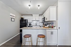 A modern kitchen with white cabinets, a granite countertop, two stools, and a black refrigerator.