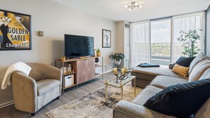 A modern living room with a sofa, armchair, and a television on a wooden cabinet. - Luxury Mid-century Condo, Cozy & Fully Remodeled. Stocked with Many Extras!  (Omaha)
