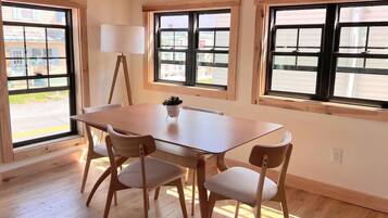 A dining area with a wooden table and chairs, large windows, and a floor lamp.