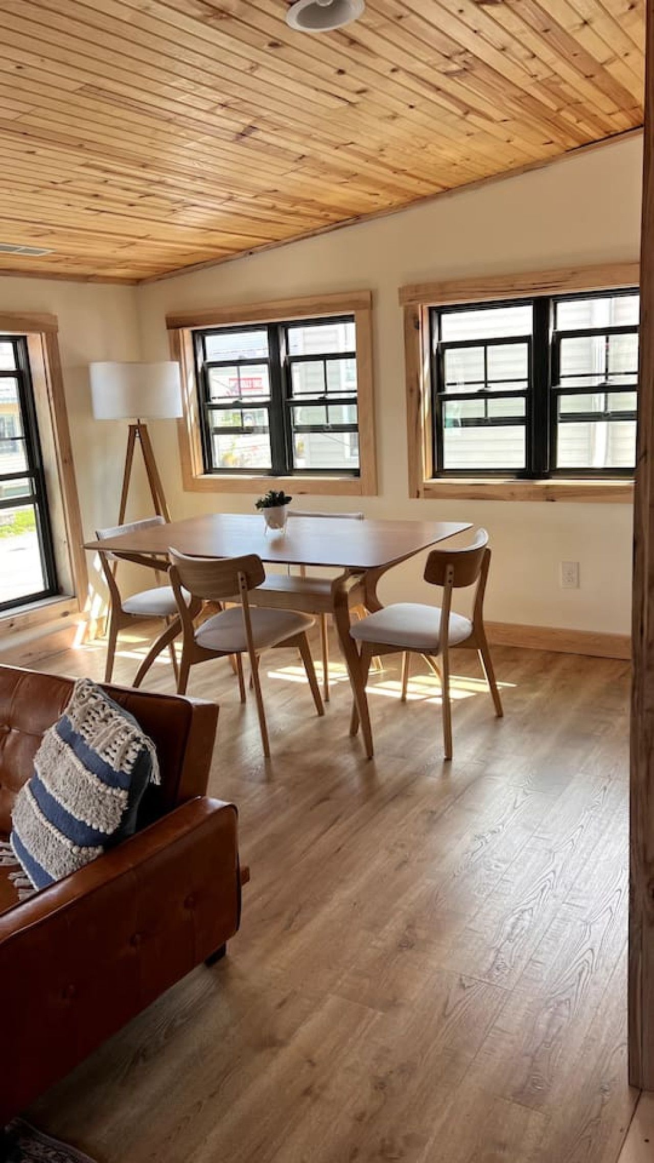 Una habitación con techo de madera, una mesa de comedor con sillas, un sofá con cojín y ventanas amplias.