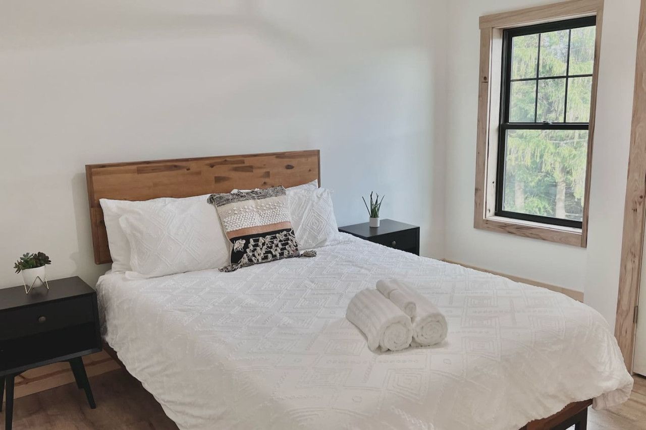A neatly made bed with a wooden headboard, white bedding, and rolled towels on the bed.