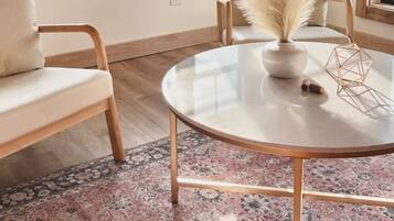 Een kamer met een ronde tafel, twee stoelen, een vloerlamp en een raam met uitzicht.