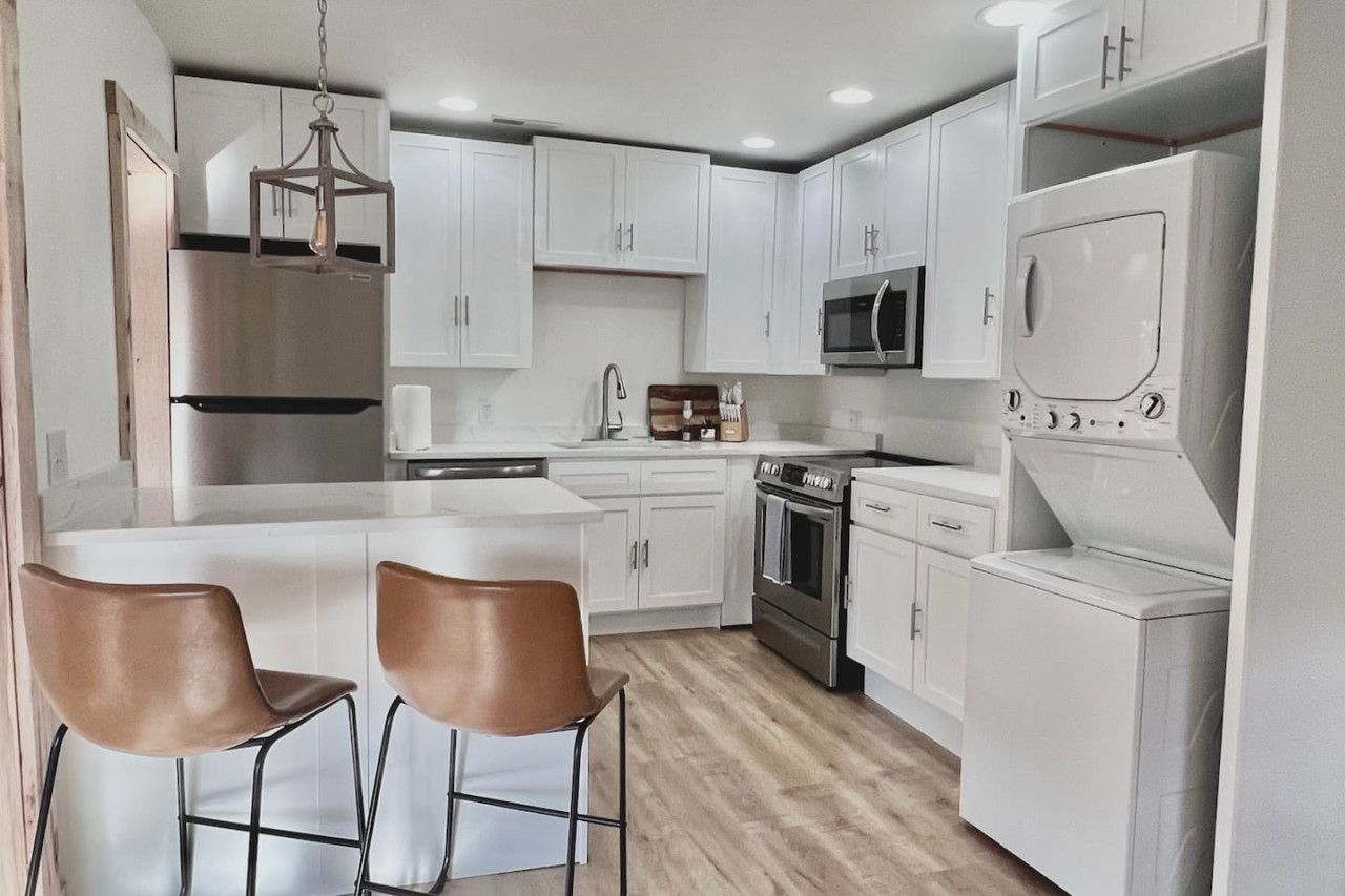A modern kitchen with white cabinets, stainless steel appliances, and a central island with two brown chairs.
