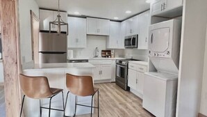 A modern kitchen with white cabinets, stainless steel appliances, and a central island with two bar stools. - Uptown - Heart of Davis (Davis)