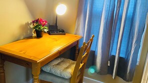 Una mesa de comedor de madera con un cojín, una pequeña planta en maceta y una lámpara de escritorio.