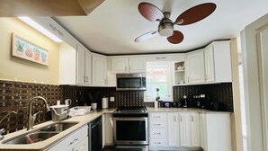 Cocina compacta con gabinetes blancos, microondas, estufa y ventilador de techo.