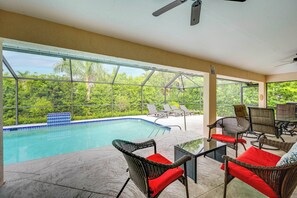 Area piscina con vista su vegetazione lussureggiante, mobili da esterno e una ventola a soffitto.
