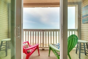 En balkon med udsigt over stranden, med to stole og et bord.