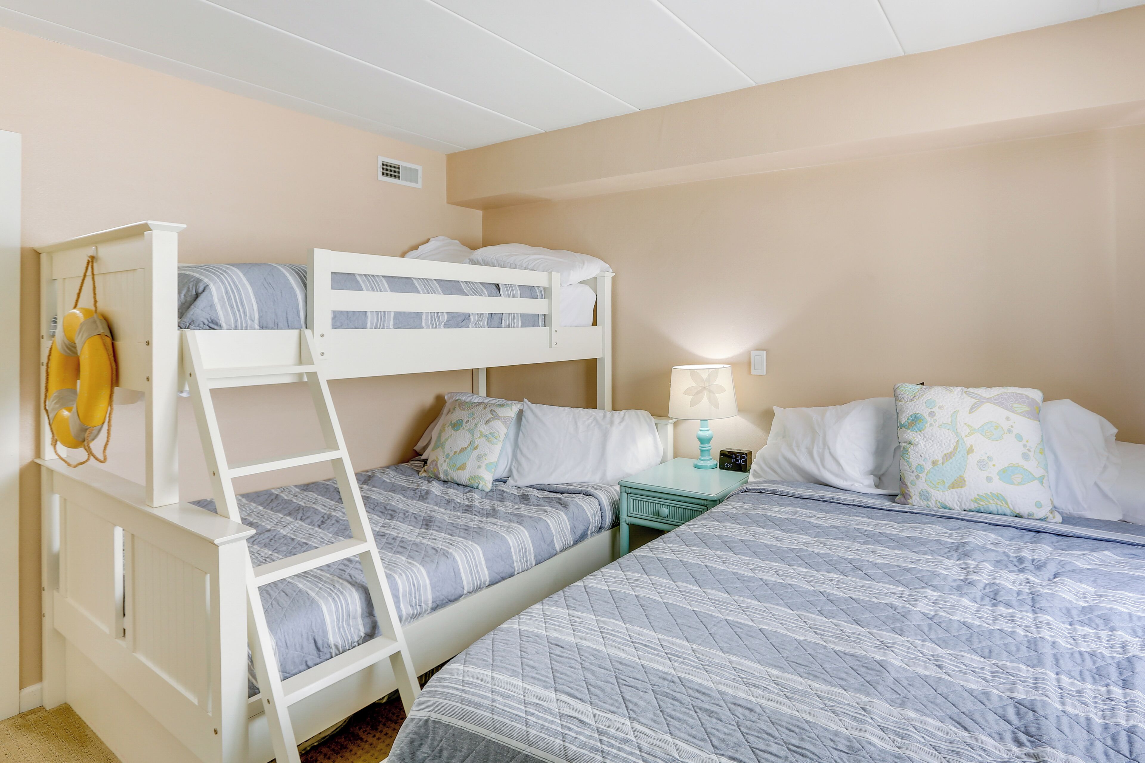 Habitación con literas, una mesita de noche con lámpara, y una cama con almohadas estampadas.
