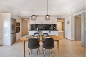 Une cuisine moderne avec des meubles blancs, un réfrigérateur en acier inoxydable et un coin repas comprenant une table en bois et des chaises noires.