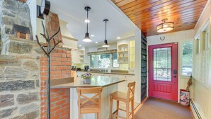Una cocina con pared de piedra, taburetes de madera y una puerta roja.