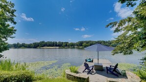 Terraza junto al lago con un muelle, sillas y una sombrilla.