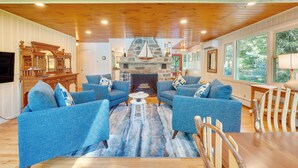 Una sala de estar acogedora con sofás azules, chimenea de piedra, techo de madera y ventanas amplias.