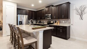 A modern kitchen with dark cabinetry, stainless steel appliances, and a granite countertop. - Magic Villa in Kissimmee with Private Pool (Kissimmee)