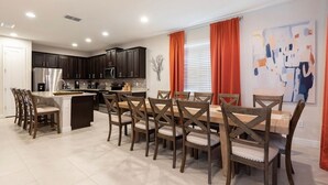 A modern kitchen with dark cabinets, a stainless steel refrigerator, and a dining area with wooden chairs and a table. - Magic Villa in Kissimmee with Private Pool (Kissimmee)