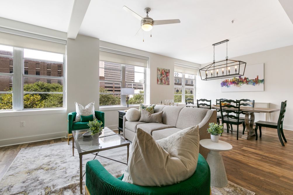 A spacious living room with a green sofa, a beige couch, and a dining area with a table and chairs.
