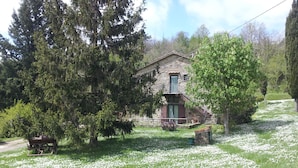 A stone building with a balcony, surrounded by trees and a grassy area with white flowers. - Exclusive Apartment With Fireplace (Castelfranco Piandisco)